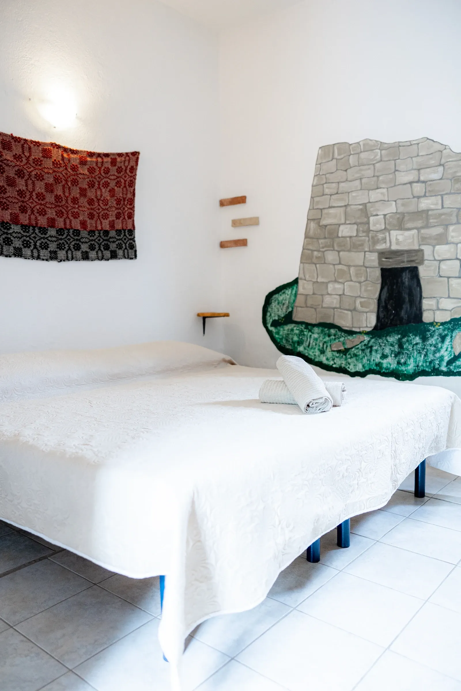 Letto matrimoniale bianco accanto a un nuraghe dipinto